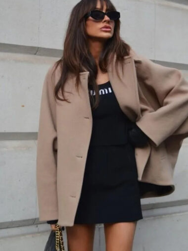 Veste cape femme ample avec col à revers beige, porté par une femme, devant un mur.