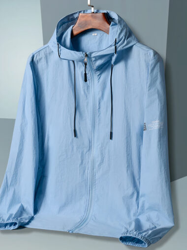 Veste coupe vent homme avec capuche, de couleur bleu clair. Posé sur un cintre sur un fond gris.