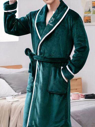 Veste d'intérieur homme style peignoir avec col rabattu portée par un homme avec un lit derrière lui et deux coussins posés dessus