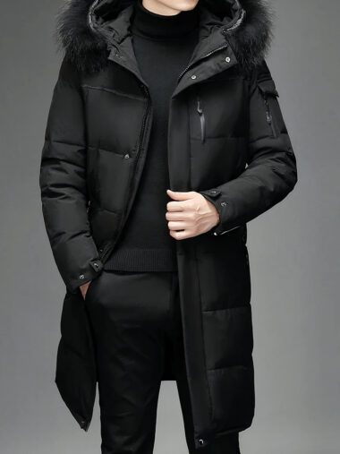 Veste doudoune homme longue et capuche en fausse fourrure portée par un homme avec un pull et un pantalon noir sur fond gris