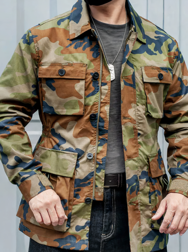 Veste saharienne homme effet camouflage militaire et coupe-vent portée par un homme avec un haut gris sur fond gris