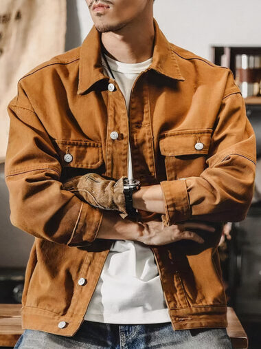 Veste saharienne homme style cargo à manche longue portée par un homme avec un t-shirt blanc et un jean bleu appuyé contre une table en bois marron