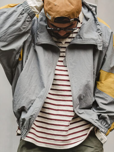 Veste vintage homme avec col haut et coupe vent, gris et jaune, porté par un homme sur un fond gris.