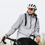 Veste vtt homme coupe-vent et imperméable, de couleur grise, porté par un homme sur son vélo, sur un fond blanc.