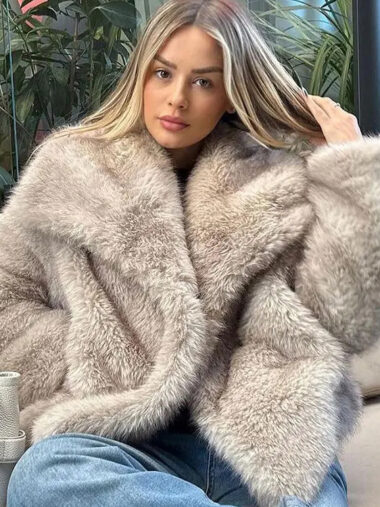 Veste habillée femme conception courte en fausse fourrure, de couleur grise, porté par une femme, assise dans un fauteuil.