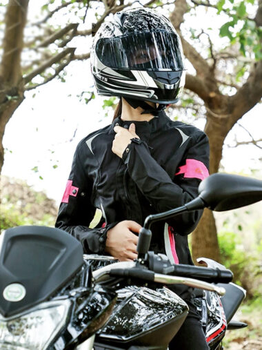 Veste moto femme avec fermeture à zipper et col haut, de couleure noire et rose, porté par une femme avec un casque sur une moto.