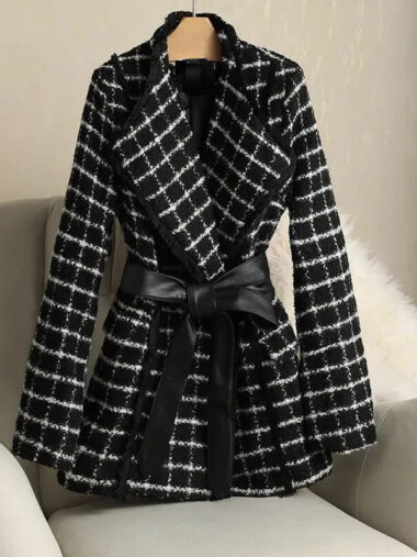 Veste habillée élégante à carreaux pour femme, de couleur noire, sur un cintre, sur un canapé.