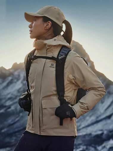 Veste randonnée femme conception respirante et imperméable, de couleur beige, porté par une femme, avec une montagne derrière elle.