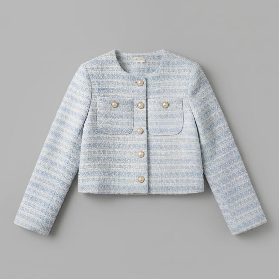 Veste style Chanel femme conception courte et élégante de couleur bleu ciel avec des boutons dorés sur fond gris.