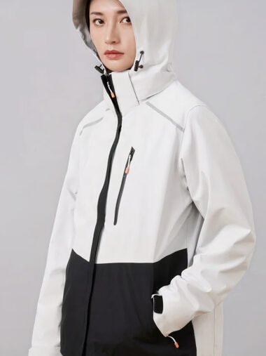 Veste de ski femme imperméable et épaisse, de couleur blanche et noire, porté par une femme, sur un fond gris.