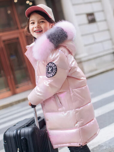 Veste fille avec capuche en fausse fourrure et écusson portée par une fille avec une casquette qui tient une valise noire dans la rue