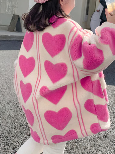 Veste fille avec des motifs de cœurs roses portée par une fille qui tient une boisson avec un pantalon blanc dans la rue