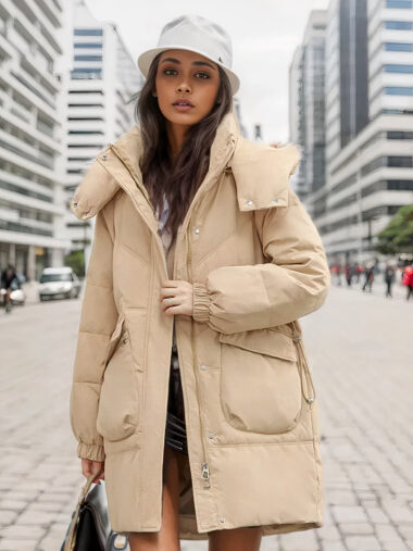 Veste parka femme rembourrée et longue portée par une femme avec un chapeau blanc et un sac dans la main qui se tient dans la rue